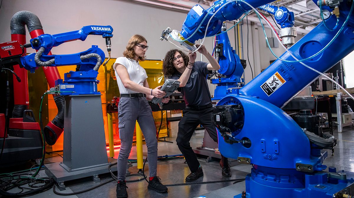 Two researchers work on a robotic armature in a lab space.
